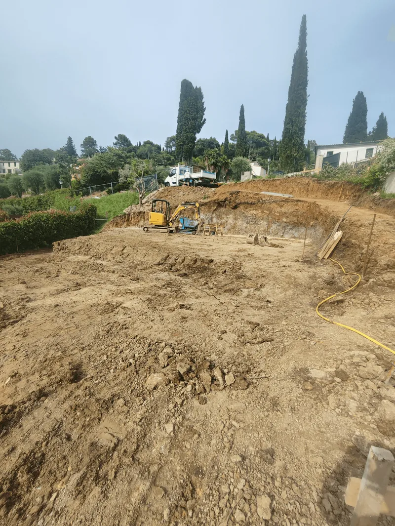 Terrain décaissé avec une petite pelle mécanique au pied d’un talus.